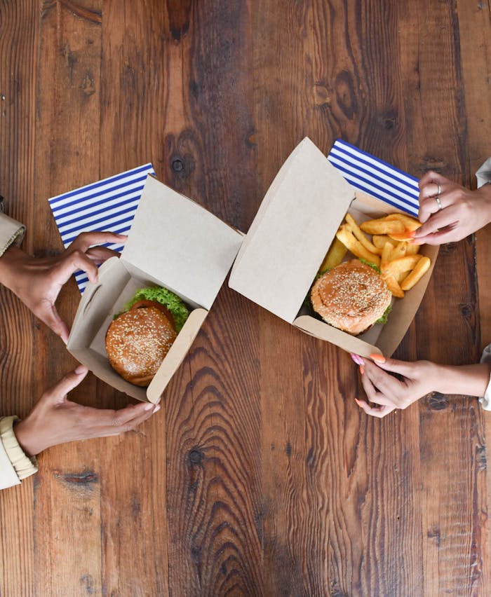 Aerial view showing two people enjoying burgers and fries on a rustic wooden table.