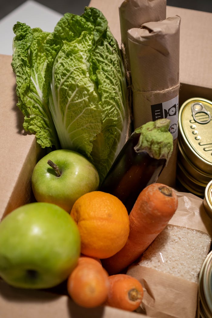 A collection of fresh fruits, vegetables, canned goods, and grains in a cardboard box.
